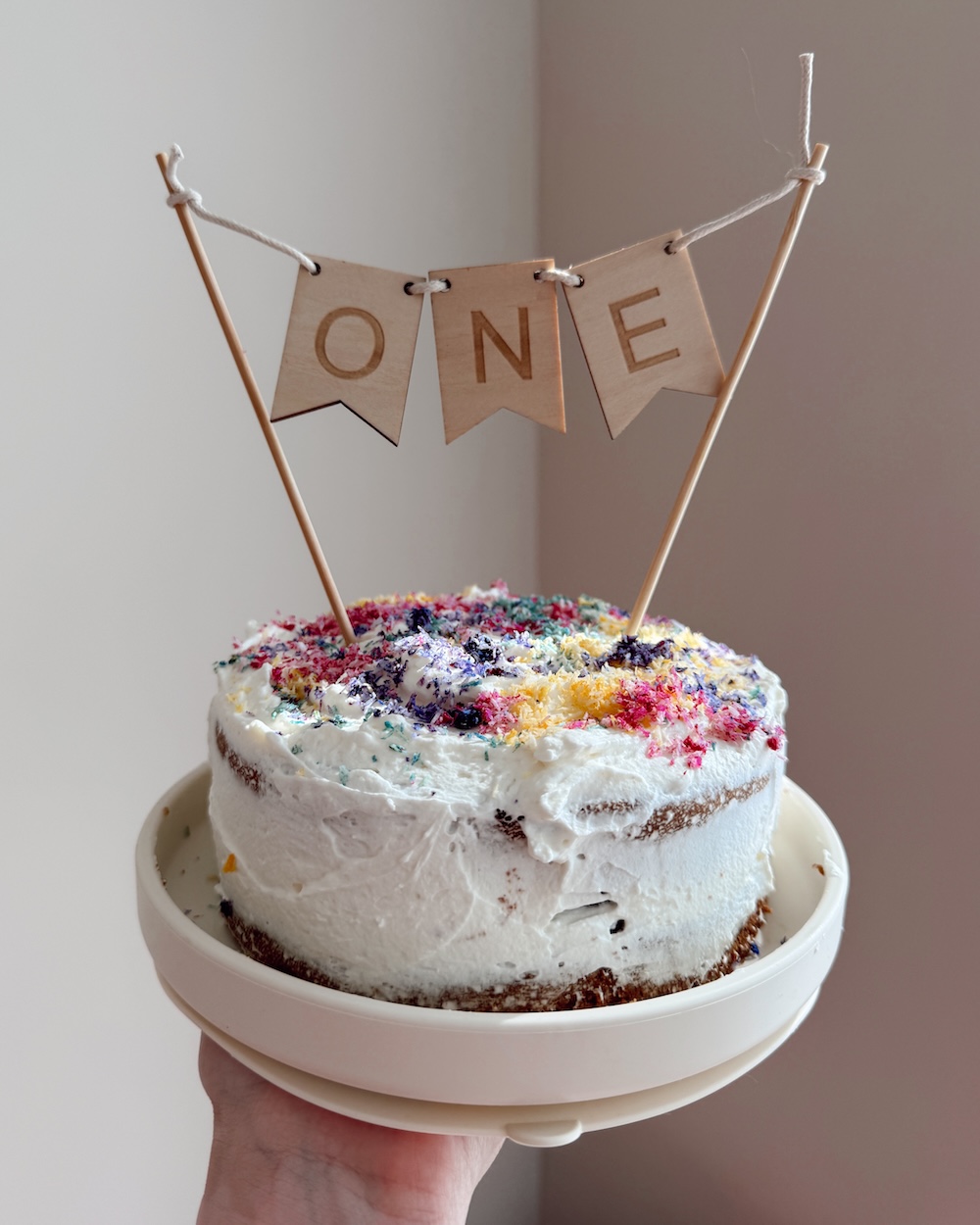Vegan Sprinkles | DIY Sugar Free Recipe A baby's first birthday smash cake decorated with rainbow coconut sprinkles and a wooden "ONE" banner topper