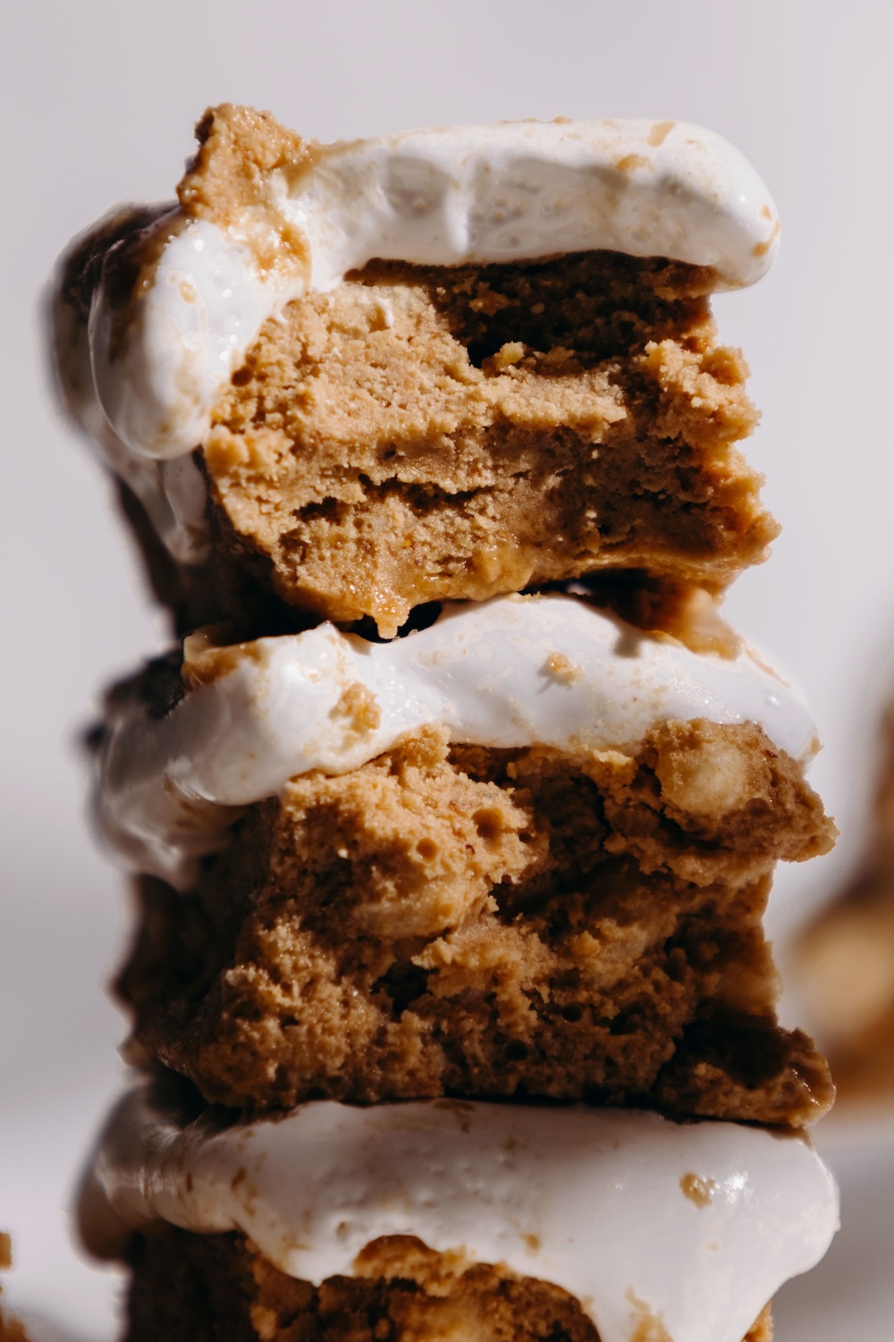 Closeup of three vegan fluffernutter protein bars stacked on parchment paper, showing a dense SunButter protein base layered with white marshmallow fluff and golden caramel drizzle