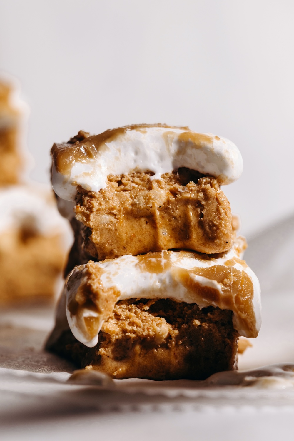 Two vegan fluffernutter protein bars stacked on parchment paper, showing a dense SunButter protein base layered with white marshmallow fluff and golden caramel drizzle
