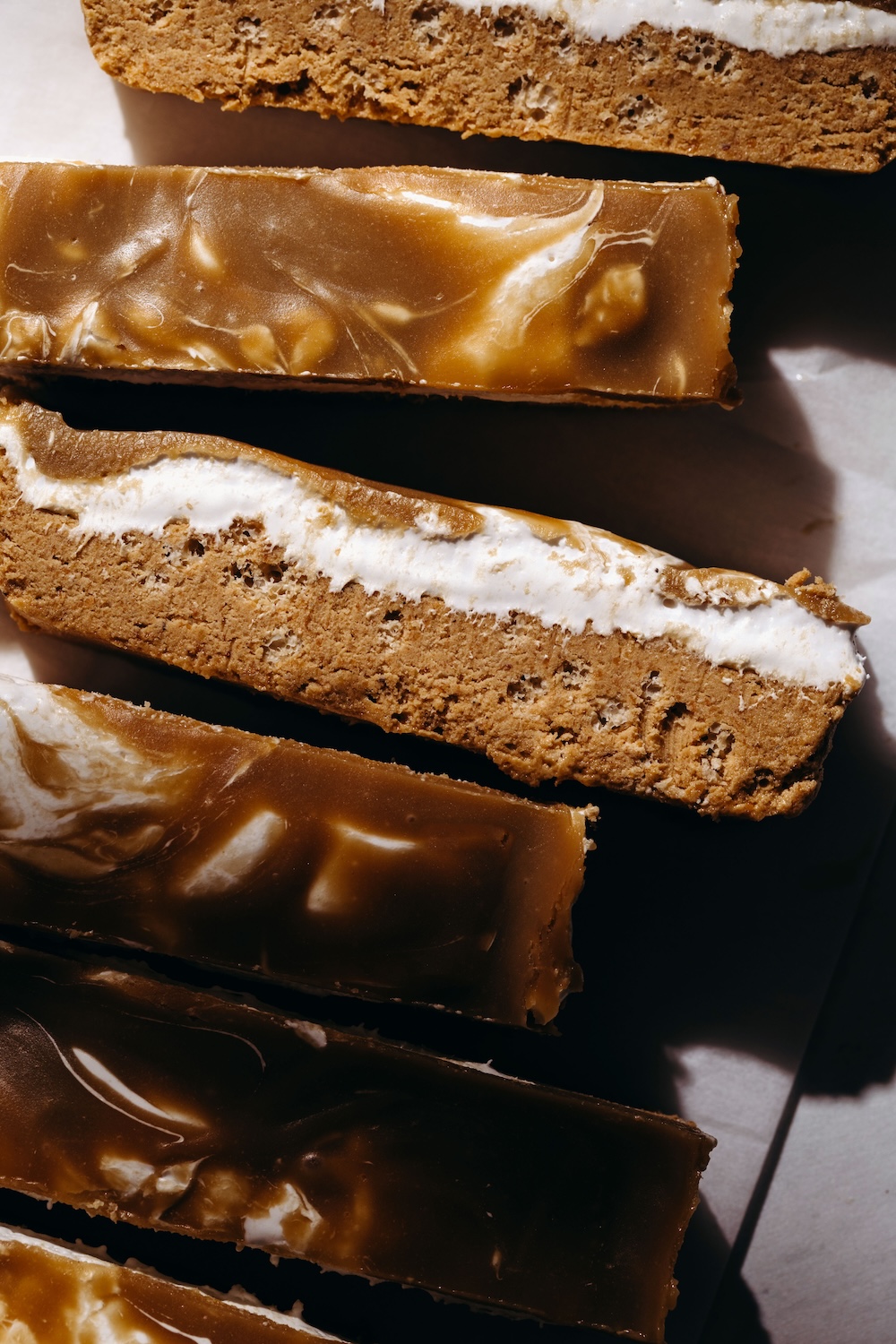 Overhead close up of sliced vegan fluffernutter protein bars scattered on parchment paper, with one bar flipped sideways to reveal the inner marshmallow fluff and SunButter protein base