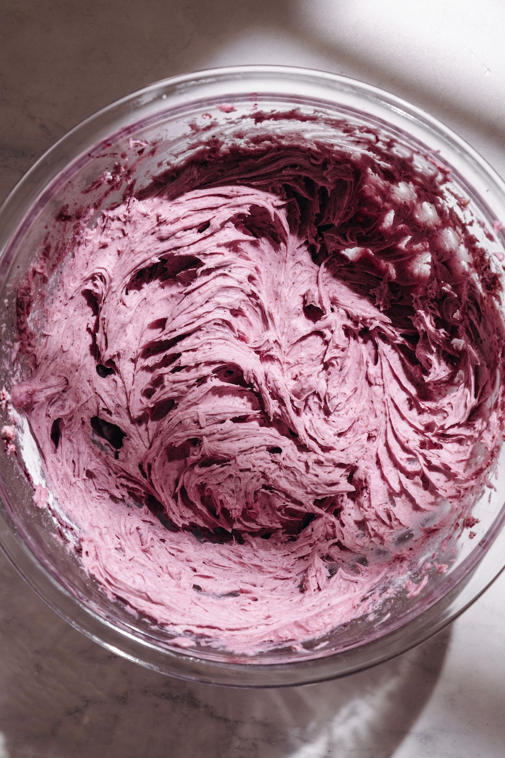 Overhead view of fresh blueberry buttercream frosting swirled in a glass mixing bowl.