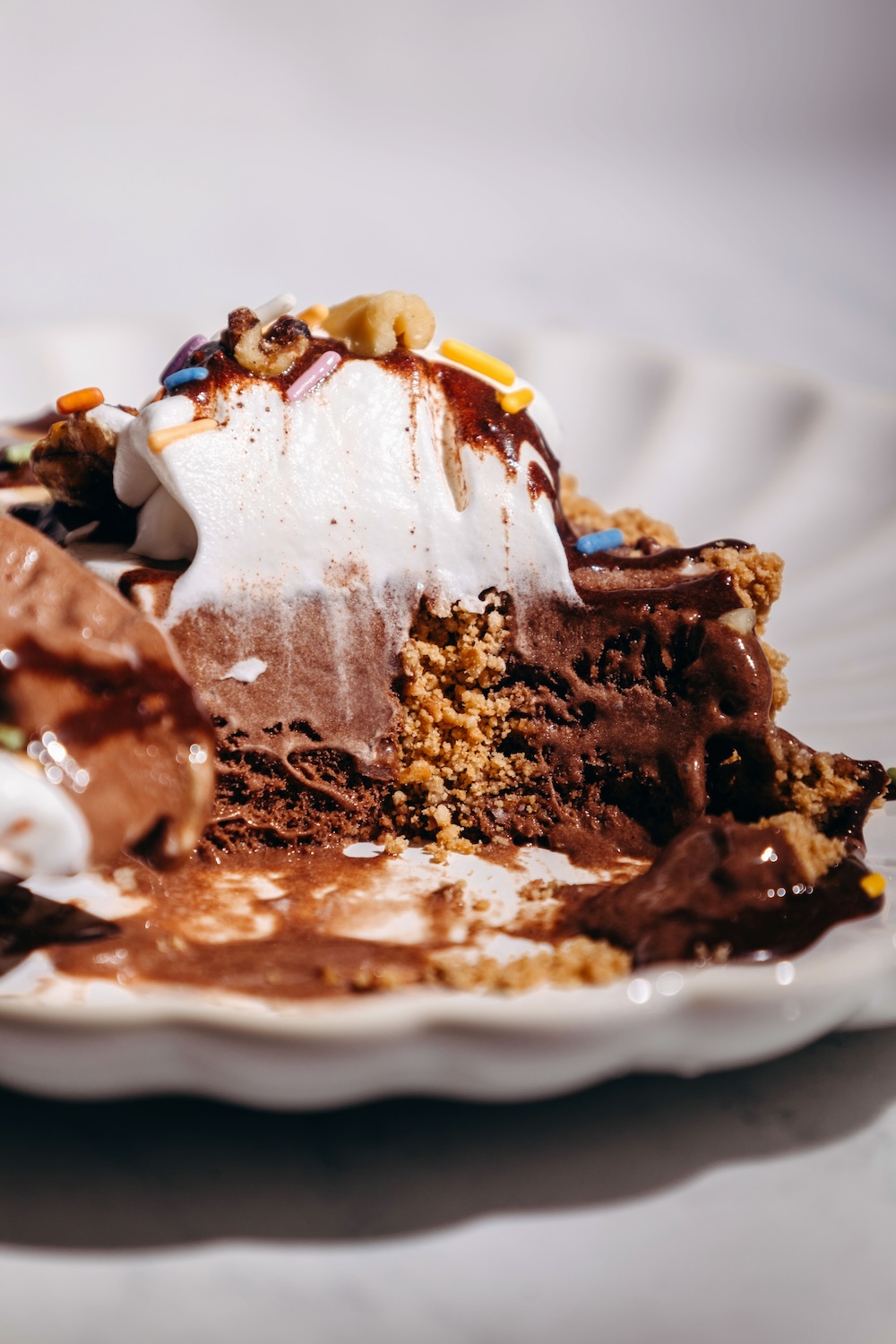 Close-up of a melting slice of no-bake dairy-free ice cream cake with whipped cream, chocolate sauce, and sugar cone crumble