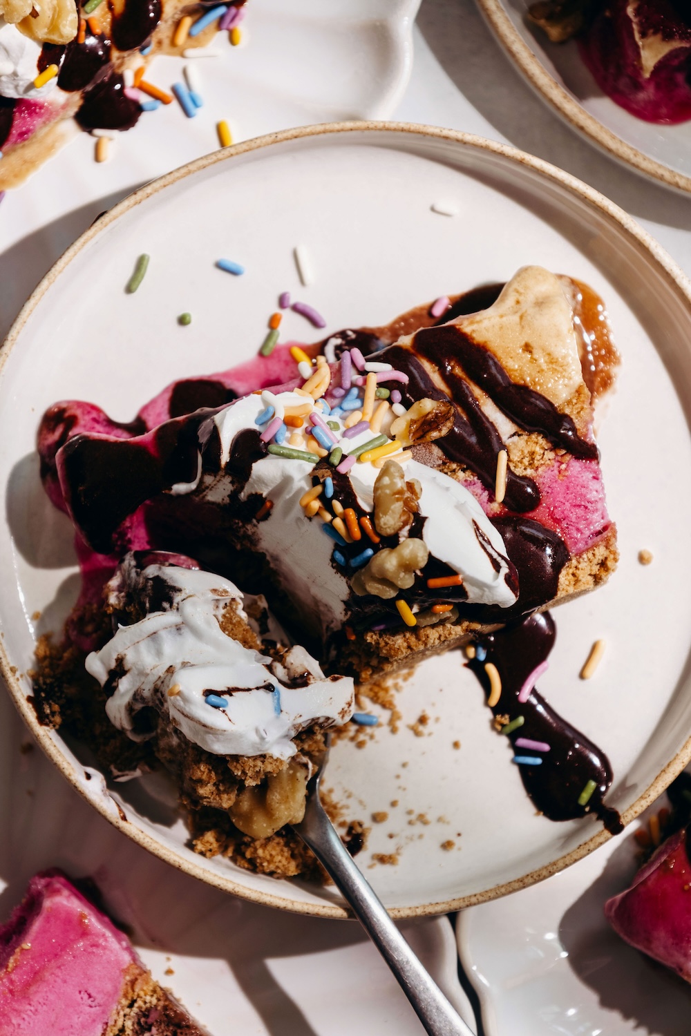 Overhead view of a no-churn loaf pan ice cream cake slice topped with whipped cream, sprinkles, walnuts, and chocolate sauce on a ceramic plate