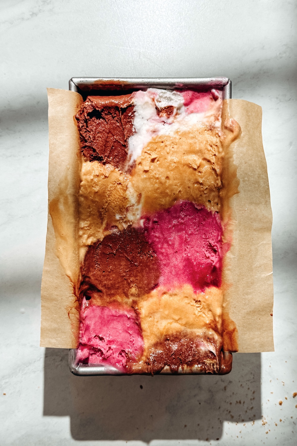 Overhead view of a vegan loaf pan ice cream cake with colorful scoops pressed into a parchment-lined pan