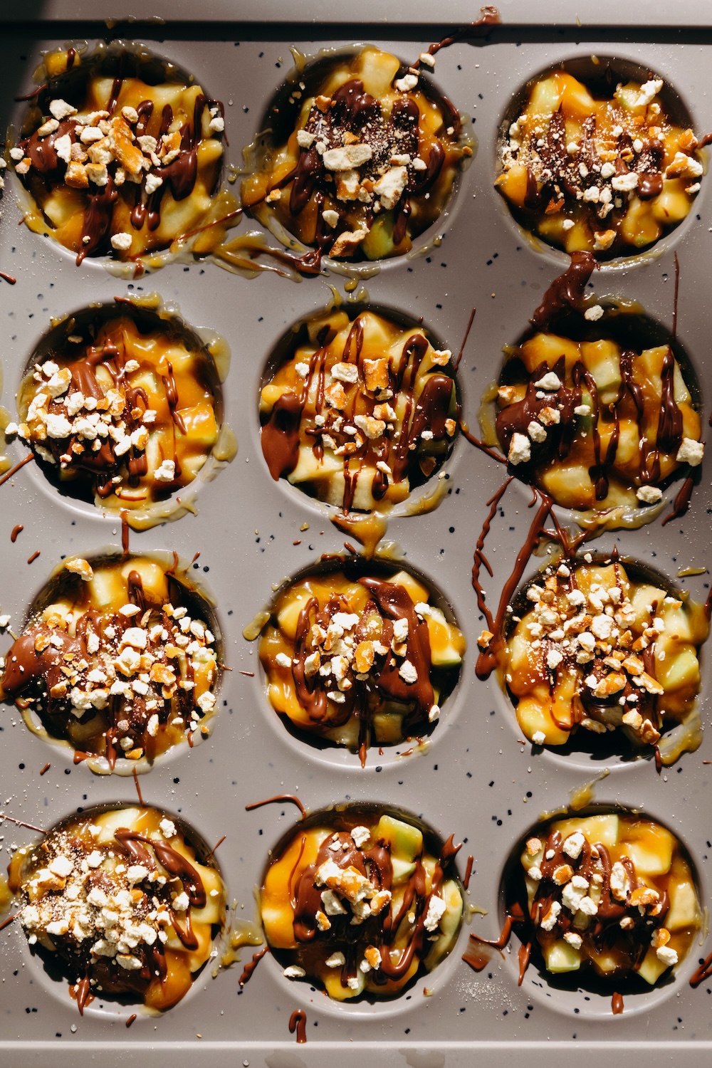 finished caramel apple pretzel bites in a mini muffin pan topped with crushed pretzels