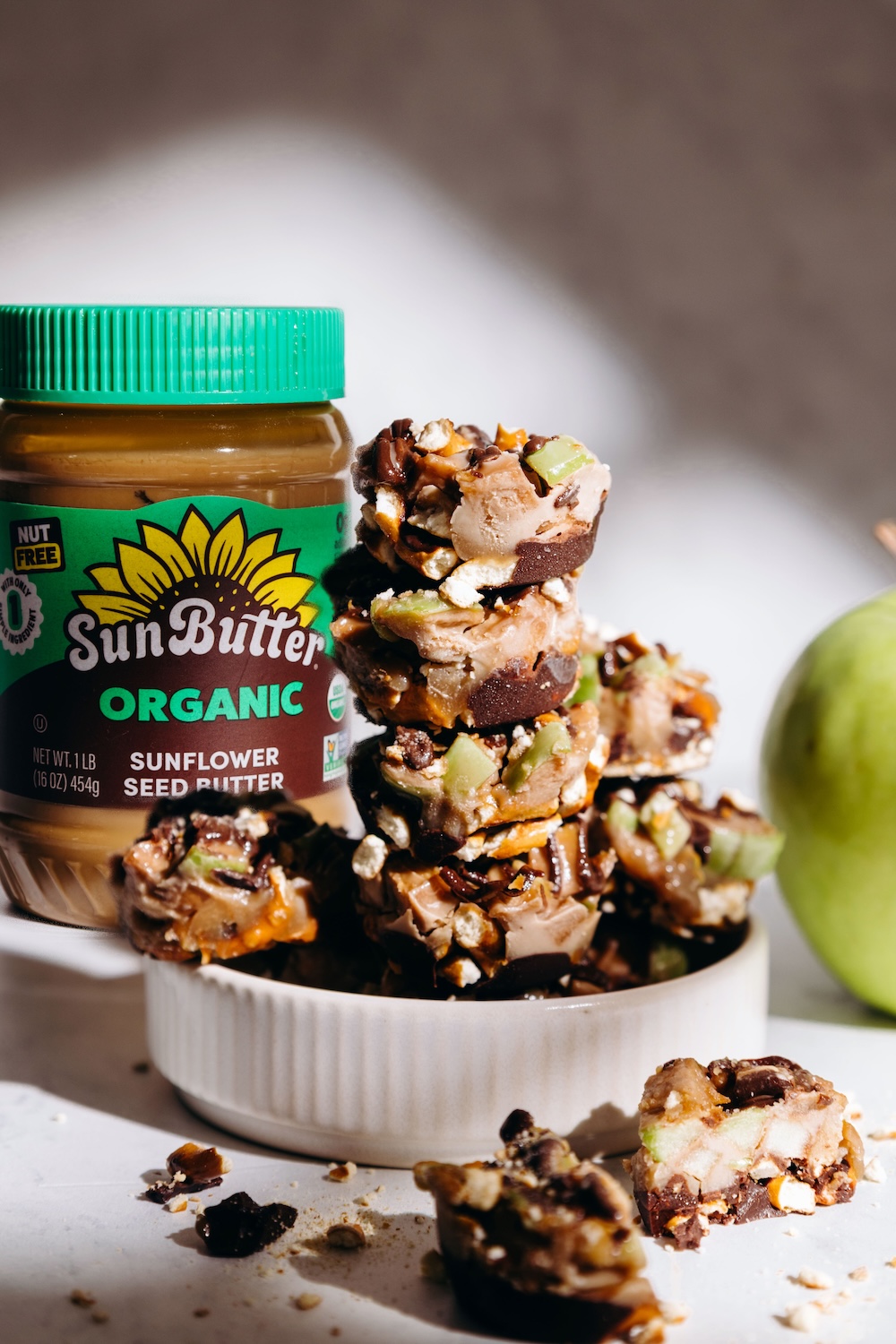 caramel apple pretzel bites stacked next to a jar of SunButter and a green apple