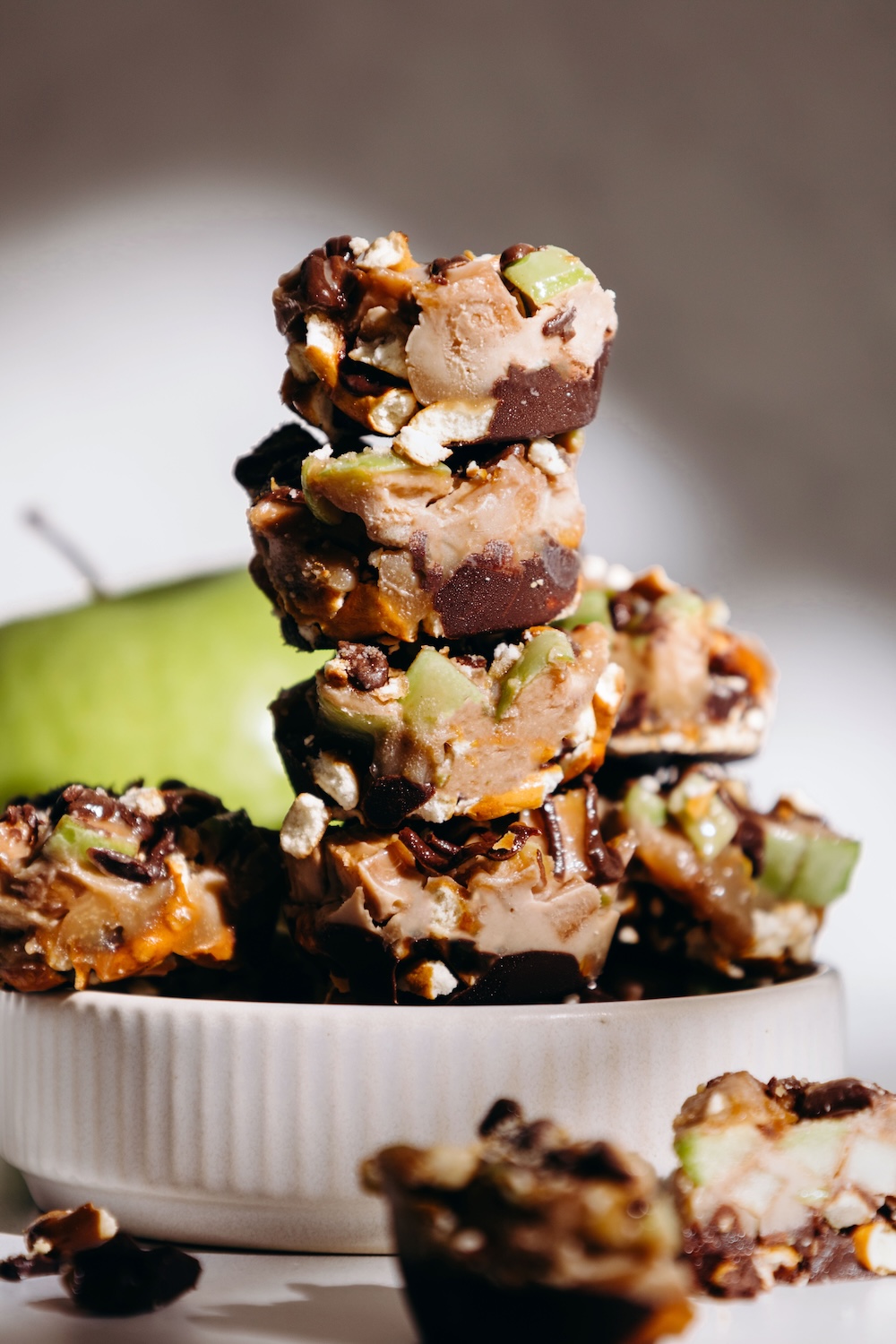 stack of caramel apple pretzel bites in a white bowl with a green apple in the background