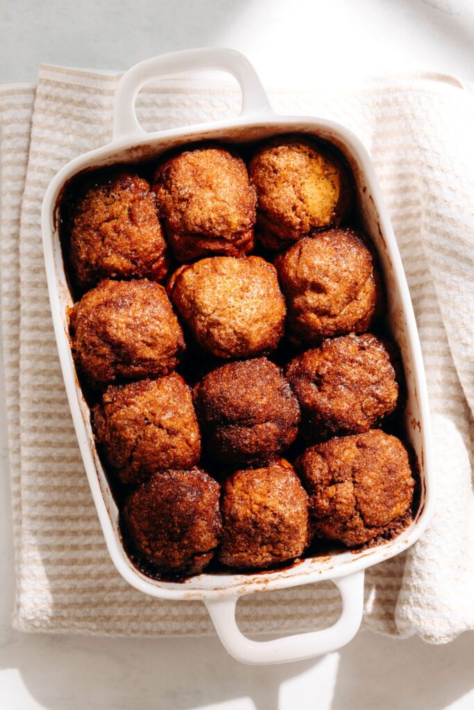 Overhead view of freshly baked pumpkin cinnamon roll bites in a white dish on a striped towel.