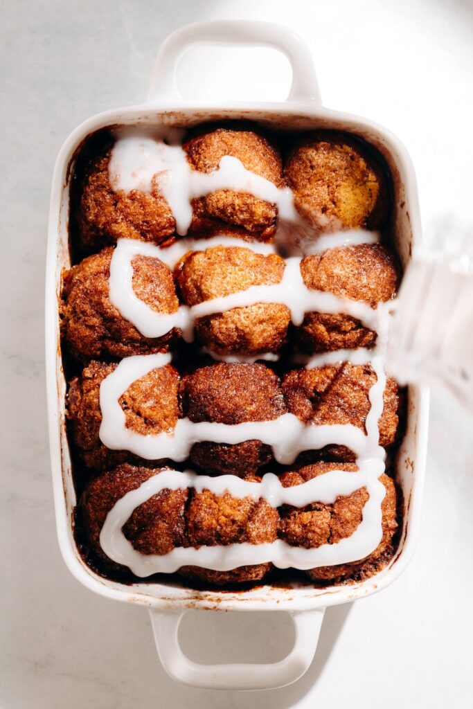 Coconut milk glaze being drizzled over baked pumpkin cinnamon roll bites.