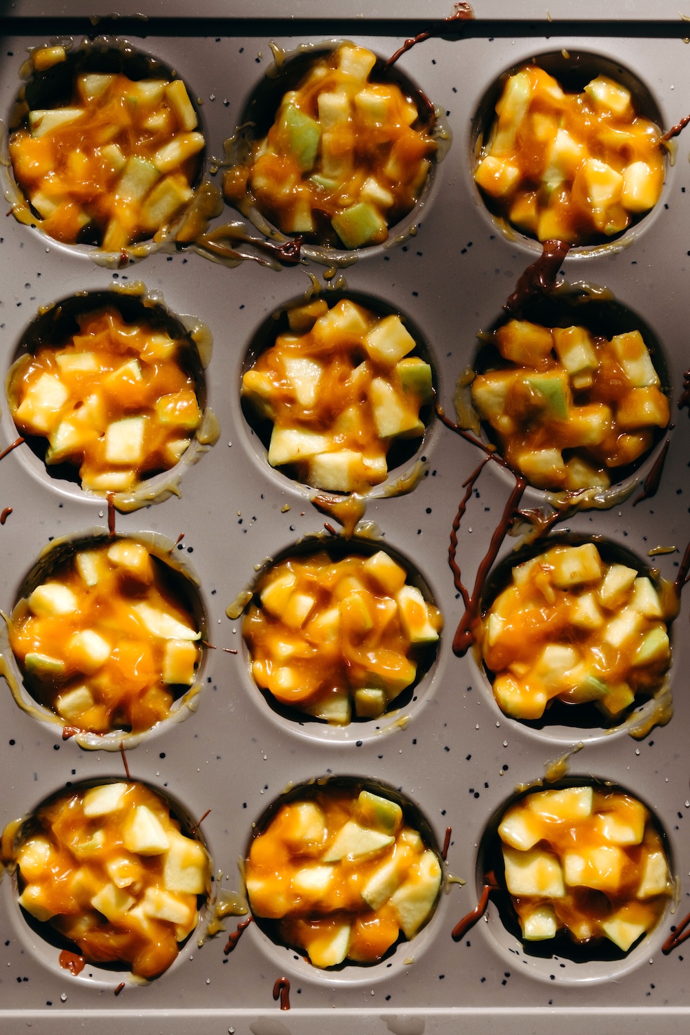 overhead mini muffin pan filled with diced apple and caramel over pretzel bases before topping