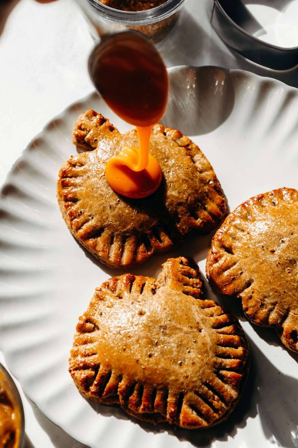 Orange glaze being spooned onto a baked pumpkin-shaped pop tart with fork-crimped edges.
