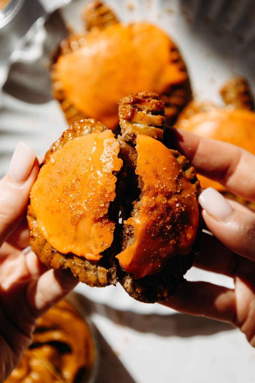 Two hands pulling apart a glazed pumpkin pie pop tart to show the soft crust inside.