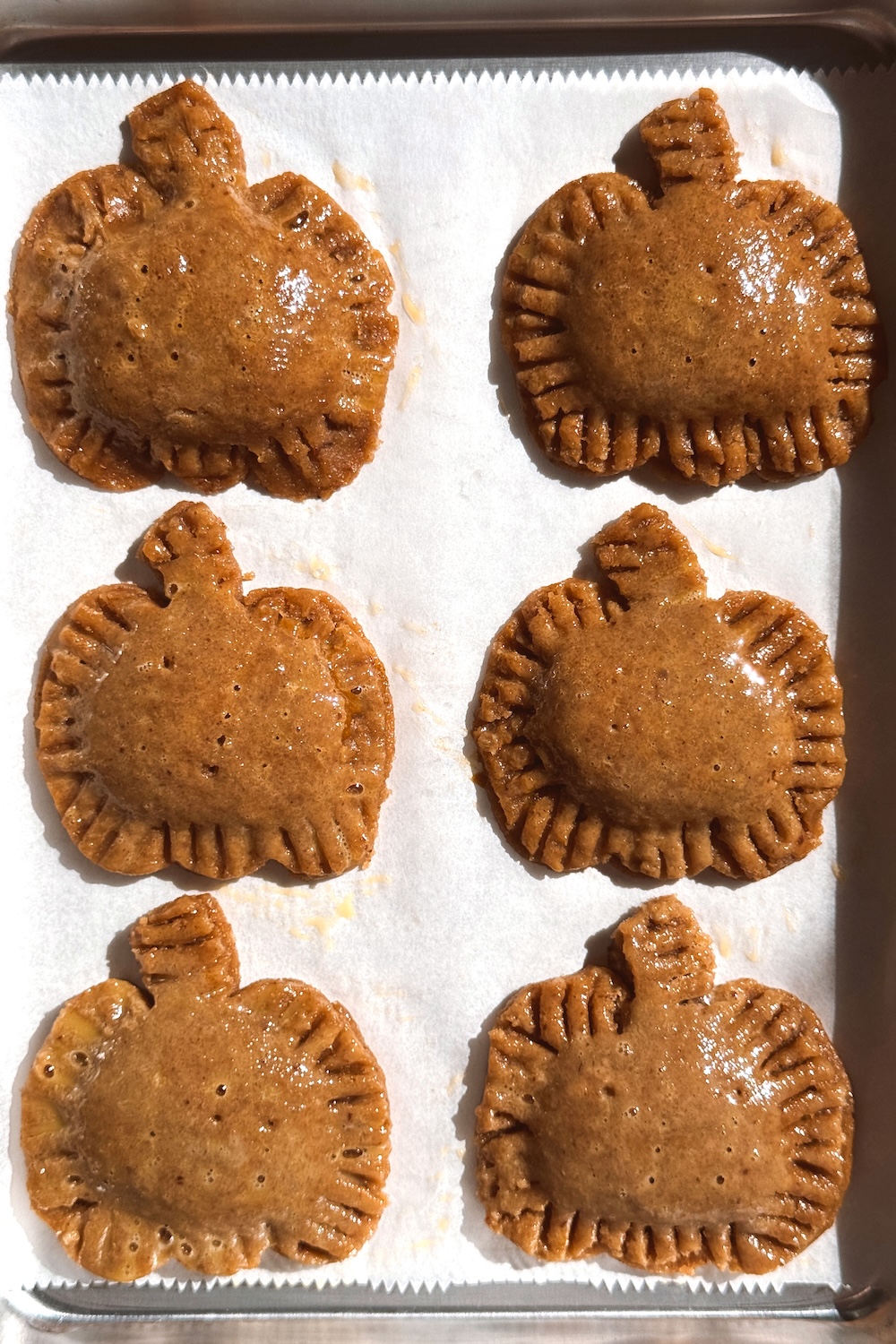 Six unbaked pumpkin-shaped pop tarts with golden crimped edges on a parchment-lined baking sheet.