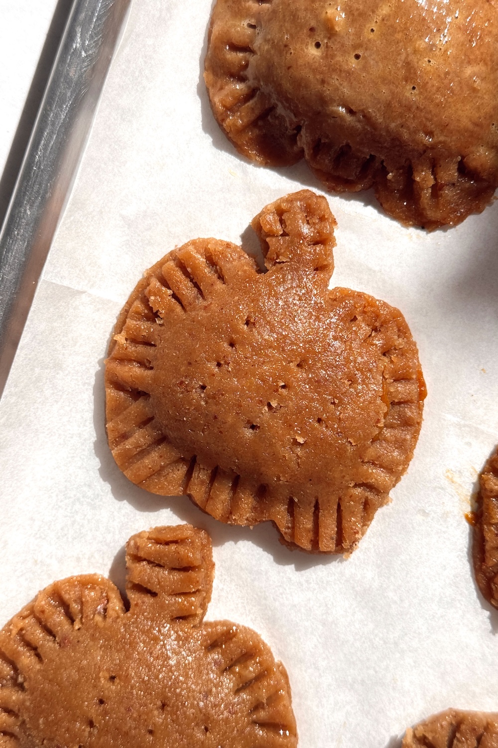 An unbaked pumpkin-shaped pop tart with fork-crimped edges on a parchment-lined baking sheet.