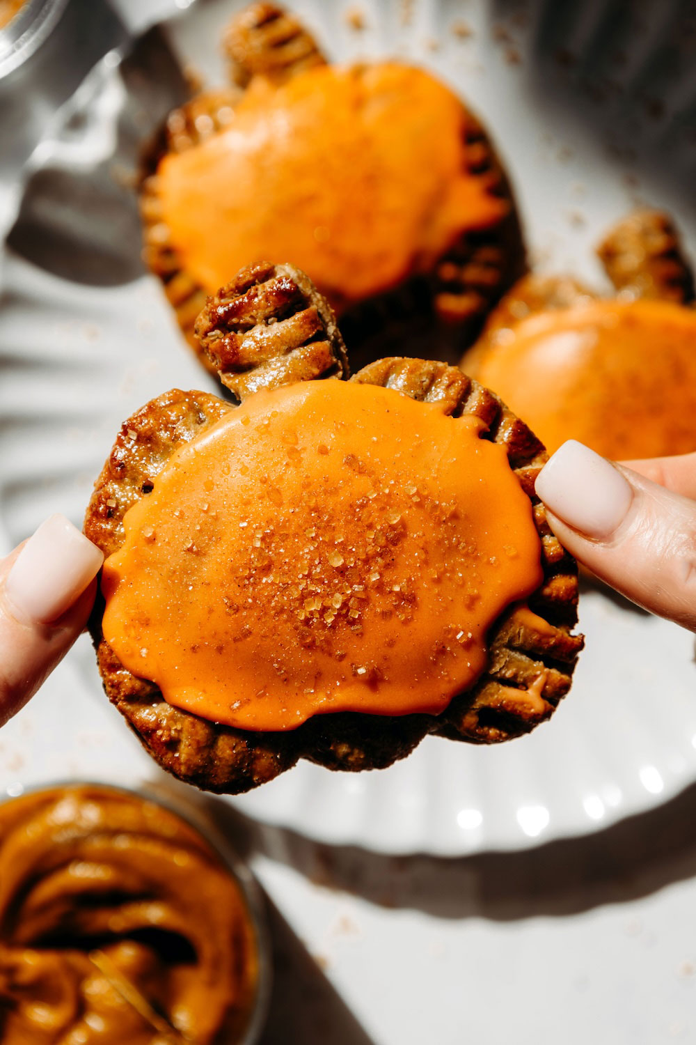A hand holding up a glazed pumpkin pie pop tart with a sugar-sprinkled orange glaze.